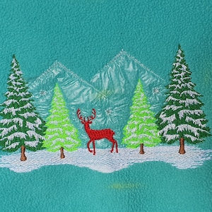 May include: Embroidered winter scene with a red deer, snow, and evergreen trees. The design includes snow-covered mountains in the background, set against a teal background. A festive, nature-themed design.