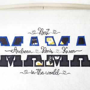 May include: Embroidered design on white fabric that reads "Best Mama in the world" with the names "Andree, Denis, Karen" embroidered above the word "Mama".