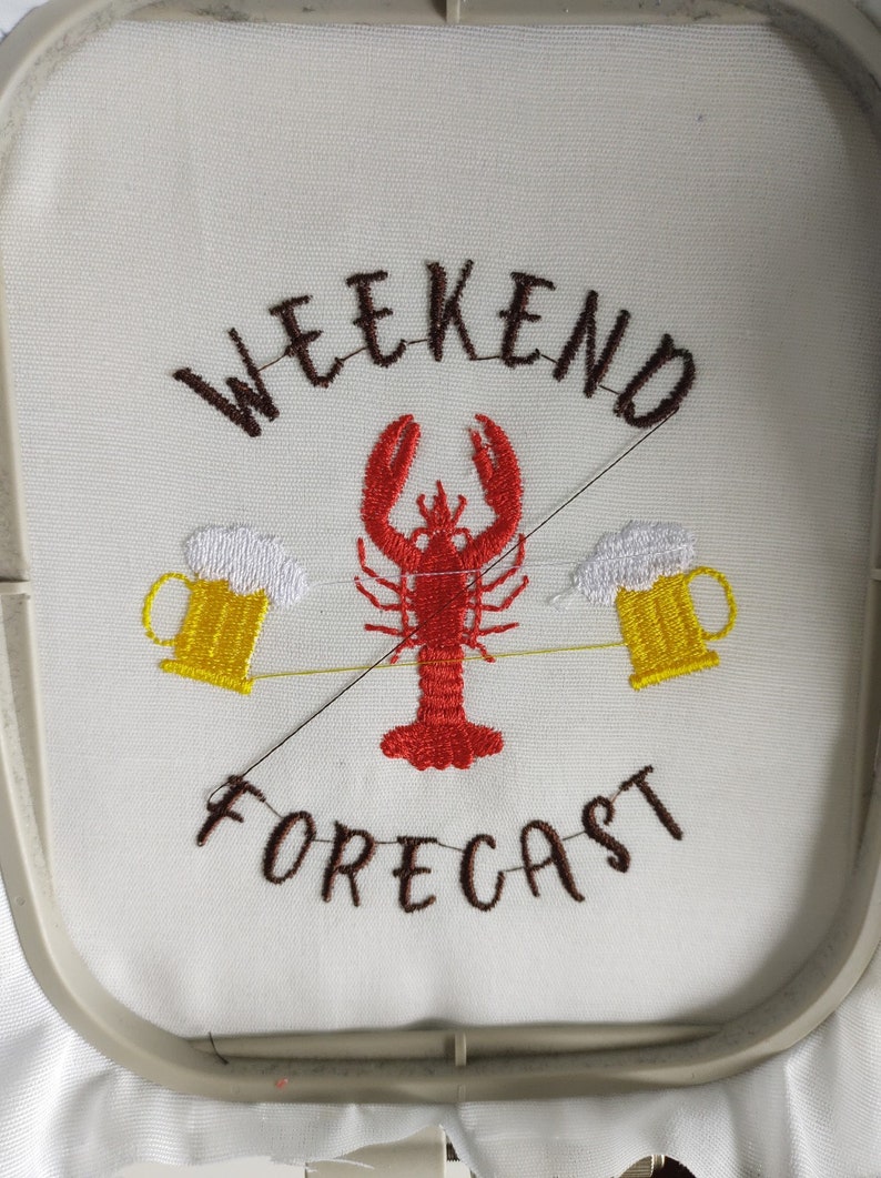 Pode incluir: Desenho bordado em tecido branco com o texto "Weekend Forecast" em fio castanho. Um lagosta vermelho est&aacute; centrado entre duas canecas de cerveja amarelas com espuma branca.