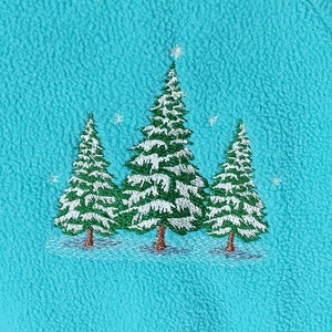 Könnte beinhalten: Gesticktes Design von drei schneebedeckten Tannen auf türkisfarbenem Stoff. Die Bäume haben grüne Nadeln und braune Stämme mit weißen Schneebesonderheiten. Ein Stern befindet sich oben auf dem mittleren Baum, und kleine Schneeflocken sind verstreut.