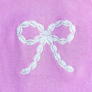 May include: A white embroidered bow on a pink ribbed fabric background.
