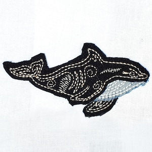 May include: Embroidered patch featuring a black orca whale with white stitching details. The whale has a white belly and intricate patterns on its body. The patch is set against a white background, highlighting the detailed craftsmanship.