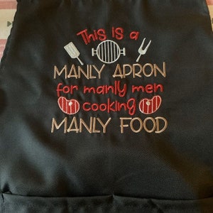 May include: Black apron with white embroidery that reads "This is a manly apron for manly men cooking manly food". The embroidery also includes a spatula, grill, and a fork.
