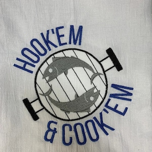 May include: White kitchen towel with blue embroidery that reads "Hook 'em & Cook 'em". The embroidery also includes a black and white illustration of a grill with two fish inside.