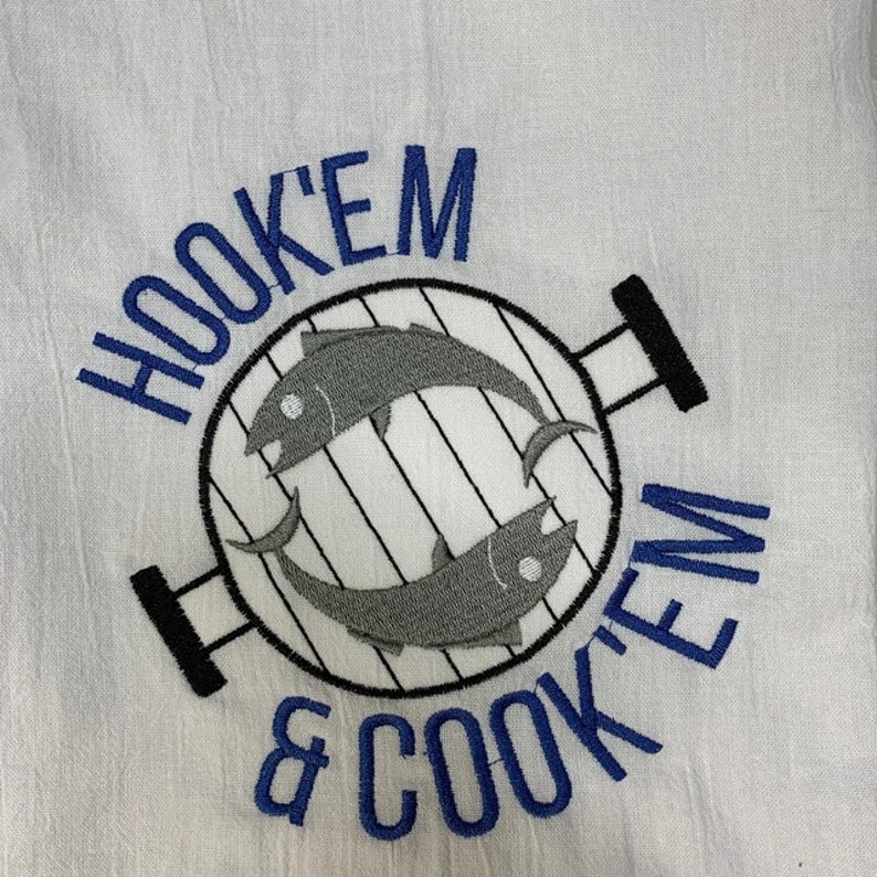 May include: White kitchen towel with blue embroidery that reads "Hook 'em & Cook 'em". The embroidery also includes a black and white illustration of a grill with two fish inside.