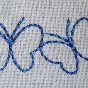 May include: A row of five blue embroidered butterflies on a white fabric background.