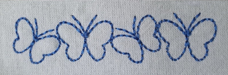 May include: A row of five blue embroidered butterflies on a white fabric background.