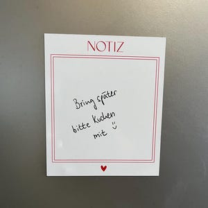 Könnte beinhalten: Ein weißer Notizzettel mit rotem Rand und dem Wort "NOTIZ" oben. Handschriftlicher Text in schwarzer Tinte lautet "Bring später bitte Kuchen mit :) ". Ein kleines rotes Herz befindet sich unten.