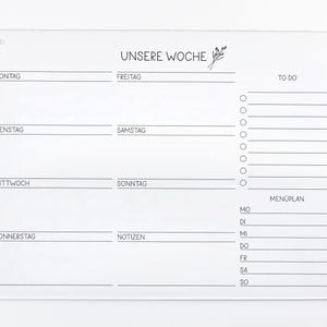 May include: A white acrylic dry erase board with a weekly planner layout. The board has sections for Monday through Sunday, a to-do list, and a meal plan. The text "UNSERE WOCHE" is at the top of the board.