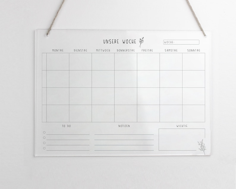 May include: A white acrylic weekly planner with black lines and text. The text says "UNSERE WOCHE" at the top and includes the days of the week in German: Montag, Dienstag, Mittwoch, Donnerstag, Freitag, Samstag, Sonntag. There are sections for "TO DO", "NOTIZEN", and "WICHTIG".