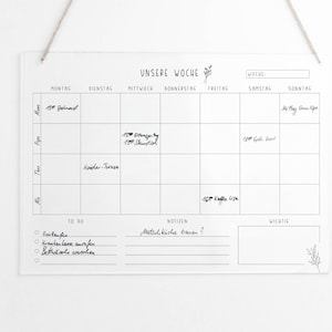 May include: A white dry-erase weekly planner with a black grid and the words "Unsere Woche" (Our Week) at the top. The planner has columns for each day of the week, with space for writing appointments and notes. There is a "To Do" list, a "Notes" section, and a "Important" section.