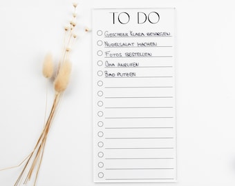 Könnte beinhalten: Ein weißes Trockenlöschboard mit schwarzem Rand und dem Schriftzug "TO DO" oben. Das Board hat eine Checkliste mit mehreren in schwarzem Marker geschriebenen Punkten, darunter "Geschenk Klara besorgen", "Nudelsalat machen", "Fotos bestellen", "Oma anrufen" und "Bad putzen".