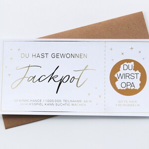 May include: A white rectangular scratch-off lottery ticket with gold foil accents. The text reads DU HAST GEWONNEN Jackpot, GEWINNCHANCE 1:1000000, TEILNAHME AB 18, GLUCKSSPIEL KANN SUCHTIG MACHEN, and BITTE HIER FREIRUBBELN with DU WIRST OPA inside.
