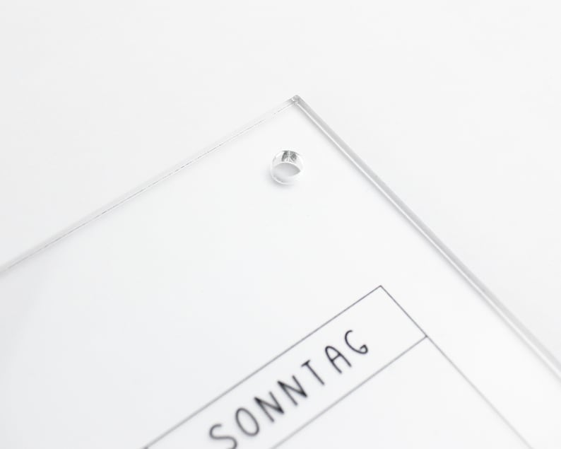 May include: A clear acrylic calendar with the word "SONNTAG" printed on it. The calendar has a hole in the top corner for hanging.