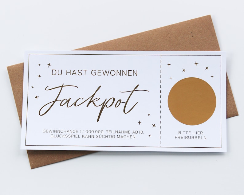 May include: A rectangular white scratch-off lottery ticket with brown text and a brown circular scratch-off area. The ticket features the text DU HAST GEWONNEN Jackpot, small star icons, and the instruction BITTE HIER FREIRUBBELN.