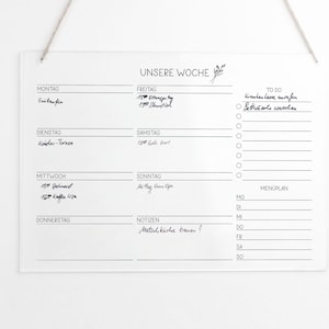 Könnte beinhalten: Ein weißes Trockenlöschboard mit schwarzem Rahmen und dem Schriftzug "UNSERE WOCHE" oben. Das Board ist in sieben Abschnitte unterteilt, einen für jeden Tag der Woche. Jeder Abschnitt hat Platz zum Schreiben von Aufgaben oder Terminen. Es gibt auch einen Abschnitt für "TO DO" und einen Abschnitt für "MENÜPLAN".