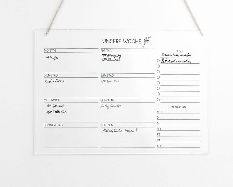 May include: A white dry-erase board with a black frame and the words "UNSERE WOCHE" at the top. The board is divided into seven sections, one for each day of the week. Each section has a space for writing tasks or appointments. There is also a section for "TO DO" and a section for "MEN&Uuml;PLAN".