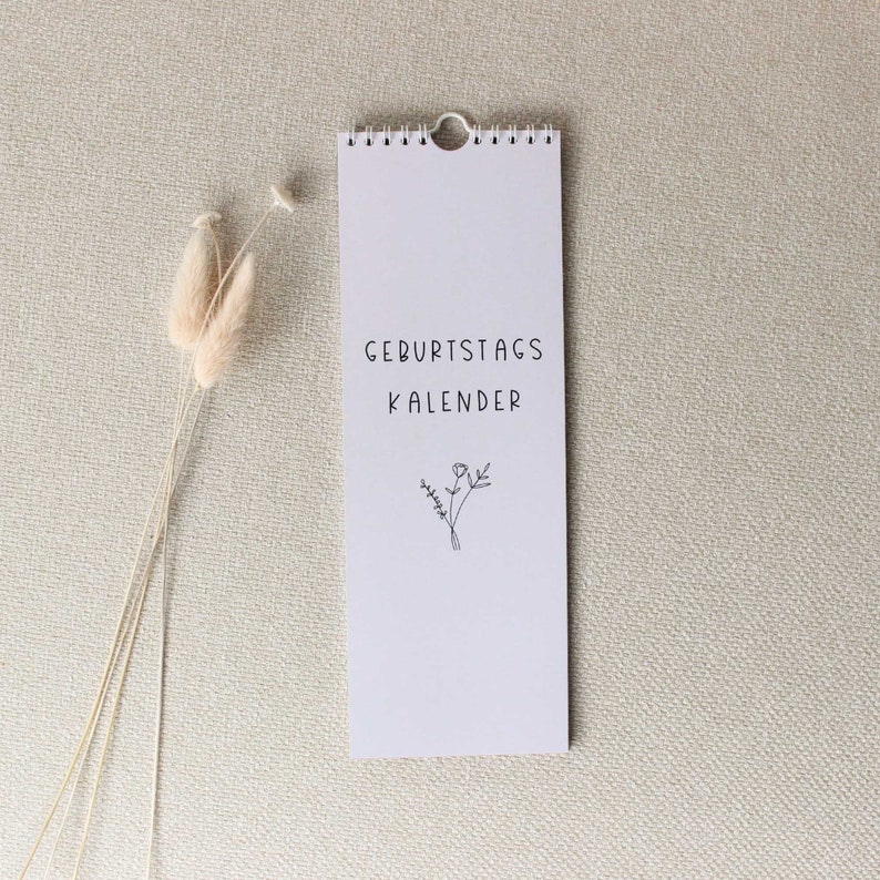 May include: A white calendar with a black floral design and the text "Geburtstagskalender" on a beige background.