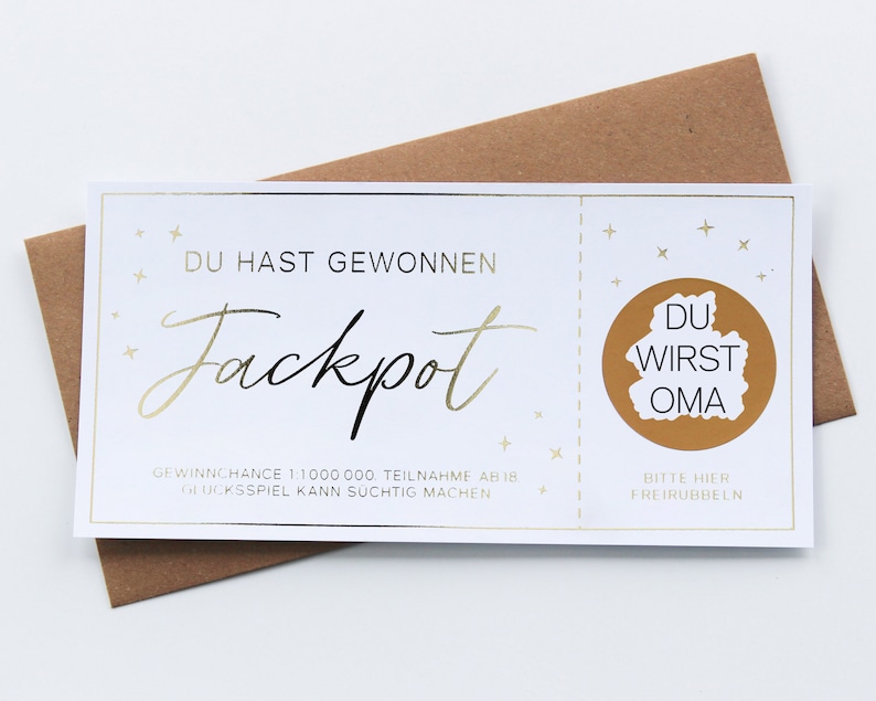 May include: A white rectangular scratch-off lottery ticket with gold foil accents and text that reads DU HAST GEWONNEN Jackpot, with a circular gold scratch-off area containing the text DU WIRST OMA, placed over a brown paper envelope.