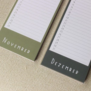 May include: A close-up of a calendar with the months November and December. The calendar is printed on green and gray paper with white text.
