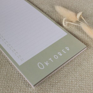 May include: A green notepad with the word "OKTOBER" printed on the front. The notepad has lined pages and is perfect for jotting down notes or making lists.