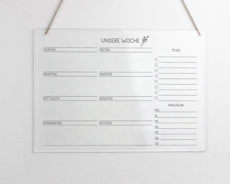 May include: A clear acrylic weekly planner with a black and white design. The planner includes sections for each day of the week, a to-do list, and a meal plan. The text "UNSERE WOCHE" is printed at the top of the planner.