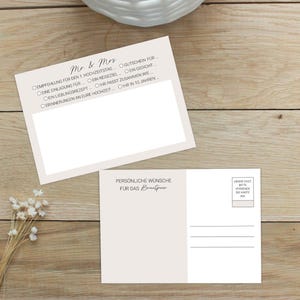 Könnte beinhalten: Zwei beige Hochzeitskarten mit deutschem Text. Eine Karte trägt die Aufschrift "Mr & Mrs" und hat Kontrollkästchen. Die andere Karte trägt die Aufschrift "PERSÖNLICHE WÜNSCHE FÜR DAS BRAUTPAAR". Die Karten liegen auf einer Holzoberfläche.