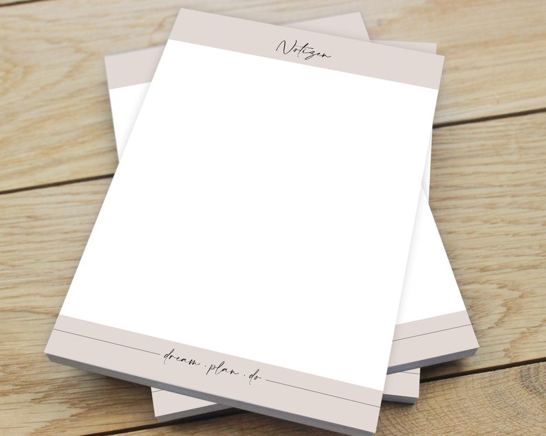 Puede incluir: Una pila de papel para bloc de notas beige y blanco con la palabra "Notizen" en la parte superior y el texto "dream plan. do." en la parte inferior.