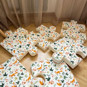 May include: A set of six foam floor cushions shaped like large jigsaw puzzle pieces. Each cushion features a white fabric cover printed with a repeating pattern of orange foxes, green maple leaves, and small orange flowers across the surface.