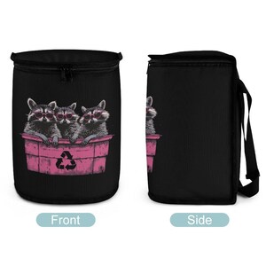 May include: A black car trash bag with a zipper closure and a shoulder strap. The front of the bag features a graphic of three raccoons wearing sunglasses in a pink trash can with a recycling symbol. The side of the bag is solid black.