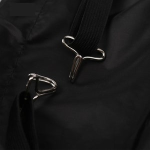 May include: Close-up of a black nylon bag with two silver metal clasps. The clasps are attached to a black strap.