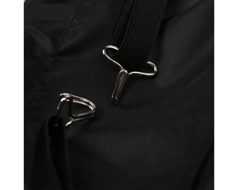 May include: Close-up of a black nylon bag with two silver metal clasps. The clasps are attached to a black strap.