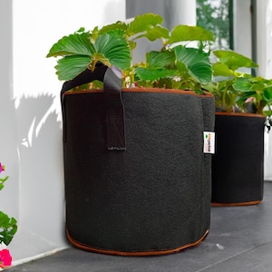 May include: Two black fabric grow bags with brown trim, one with a brown handle, filled with green plants. The bags have a white label with the text "GrowItGreen" on them.