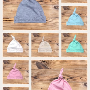 May include: A collection of ten baby hats in various colors, including blue, pink, white, gray, and black. Each hat has a knot on top and the text "Playtime Blanks" printed on the bottom.
