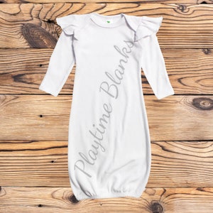 May include: White long-sleeved baby gown with ruffled sleeves. The gown has a gathered bottom and is made of a soft, stretchy fabric. The text "Playtime Blanks" is printed on the gown.