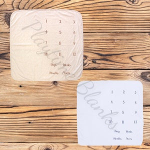 May include: Two white baby blankets with a grid of numbers 1-12 and the words "Days", "Weeks", "Months", and "Years" printed on them. The blankets are on a wooden surface.