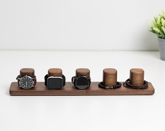May include: A wooden watch and bracelet stand with five slots. The stand is made of dark walnut wood and has a smooth, polished finish. There are three watches and two bracelets on the stand.