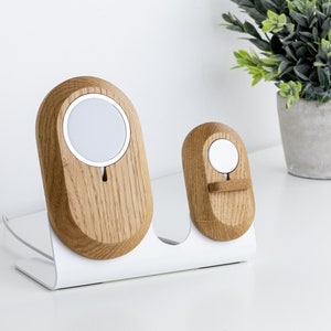 Può includere: Un supporto bianco con due stazioni di ricarica in legno per Apple Watch. La stazione più grande ha un anello di ricarica bianco e la stazione più piccola ha un supporto in legno marrone.