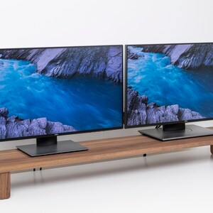 May include: Two black computer monitors with a blue and gray landscape image displayed on the screen. The monitors are sitting on a wooden stand.