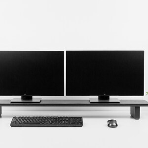 Puede incluir: Un soporte de monitor negro con dos monitores negros en la parte superior. Un teclado y un rat&oacute;n negros est&aacute;n en el escritorio blanco debajo del soporte. Una peque&ntilde;a planta en maceta est&aacute; en el lado derecho del escritorio.