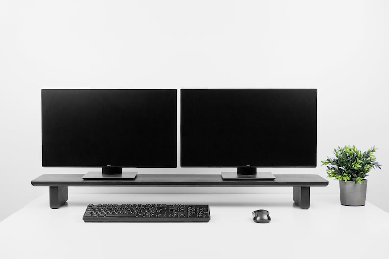 Puede incluir: Un soporte de monitor negro con dos monitores negros en la parte superior. Un teclado y un rat&oacute;n negros est&aacute;n en el escritorio blanco debajo del soporte. Una peque&ntilde;a planta en maceta est&aacute; en el lado derecho del escritorio.