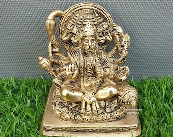 Könnte beinhalten: Eine goldfarbene Messingstatue von Hanuman, einer hinduistischen Gottheit, mit vier Gesichtern und vier Armen. Die Statue sitzt auf einem Sockel mit aufwendigen Details. Die Statue steht auf einem grünen Grasgrund.