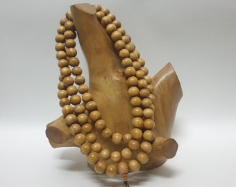 May include: A wooden mala bead necklace with brown beads and a black tassel. The necklace is displayed on a wooden stand.