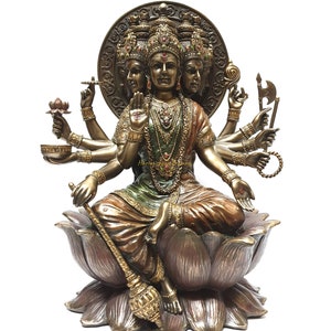 May include: A gold-toned statue of a deity with multiple arms and heads, sitting on a lotus flower. The deity is adorned with intricate jewelry and a crown. The statue is made of metal and has a detailed finish.
