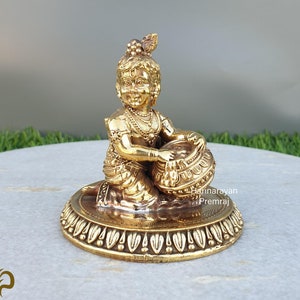 May include: A gold-colored statue of a young boy playing a drum. The statue is sitting on a round base with decorative details.