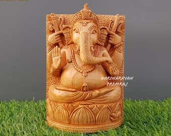 Op de afbeelding: Een handgesneden houten beeld van de hindoe-god Ganesha. Het beeld is ingewikkeld gedetailleerd en toont Ganesha zittend op een lotusthron met zijn slurf omhoog en zijn handen in een zegenende houding. Het beeld is gemaakt van lichtbruin hout en heeft een natuurlijke afwerking.