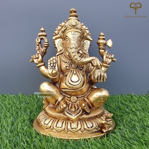 Puede incluir: Una estatua de bronce dorada de Ganesha, el dios hind&uacute; de la sabidur&iacute;a y la prosperidad, sentado sobre una base de loto. La estatua est&aacute; intrincadamente detallada y presenta a Ganesha con su cabeza de elefante, cuatro brazos y un colmillo roto.