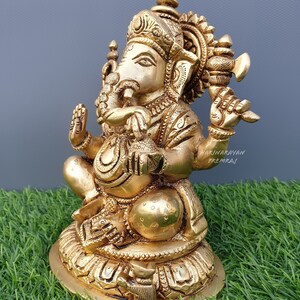 Puede incluir: Una estatua de metal dorada de Ganesha, el dios hind&uacute; de la sabidur&iacute;a y la prosperidad. La estatua est&aacute; sentada sobre una base de loto y sostiene un peque&ntilde;o hacha en una mano y un dulce en la otra. La estatua est&aacute; intrincadamente detallada y tiene un dise&ntilde;o tradicional indio.