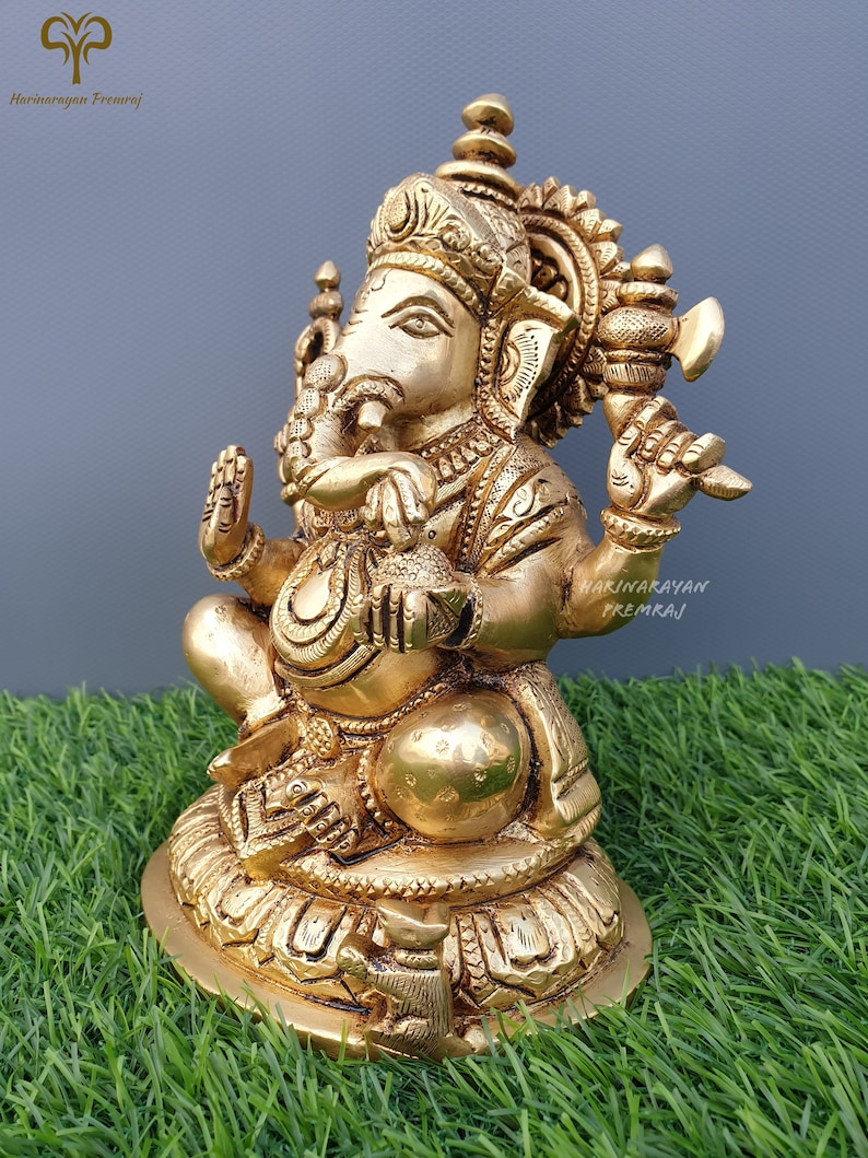 Puede incluir: Una estatua de metal dorada de Ganesha, el dios hind&uacute; de la sabidur&iacute;a y la prosperidad. La estatua est&aacute; sentada sobre una base de loto y sostiene un peque&ntilde;o hacha en una mano y un dulce en la otra. La estatua est&aacute; intrincadamente detallada y tiene un dise&ntilde;o tradicional indio.