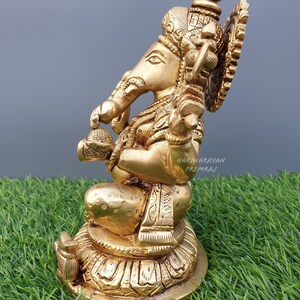 Puede incluir: Una estatua de bronce dorada de Ganesha, el dios hind&uacute; de la sabidur&iacute;a y la prosperidad, sentado sobre una base de loto. La estatua est&aacute; intrincadamente detallada con tallas ornamentadas y una corona en la cabeza de Ganesha.